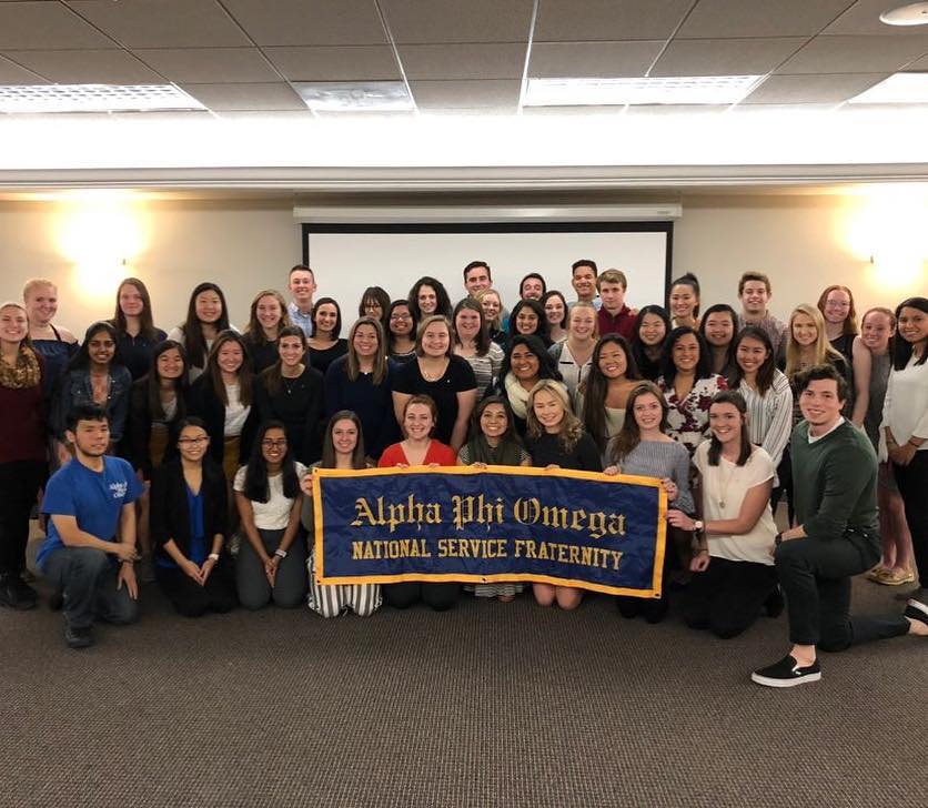 The Omega Epsilon chapter of Alpha Phi Omega at Illinois Wesleyan University poses as a group following a ceremony in Fall 2018. The members in the front row hold a blue banner with a gold border and lettering that reads "Alpha Phi Omega National Service Fraternity"